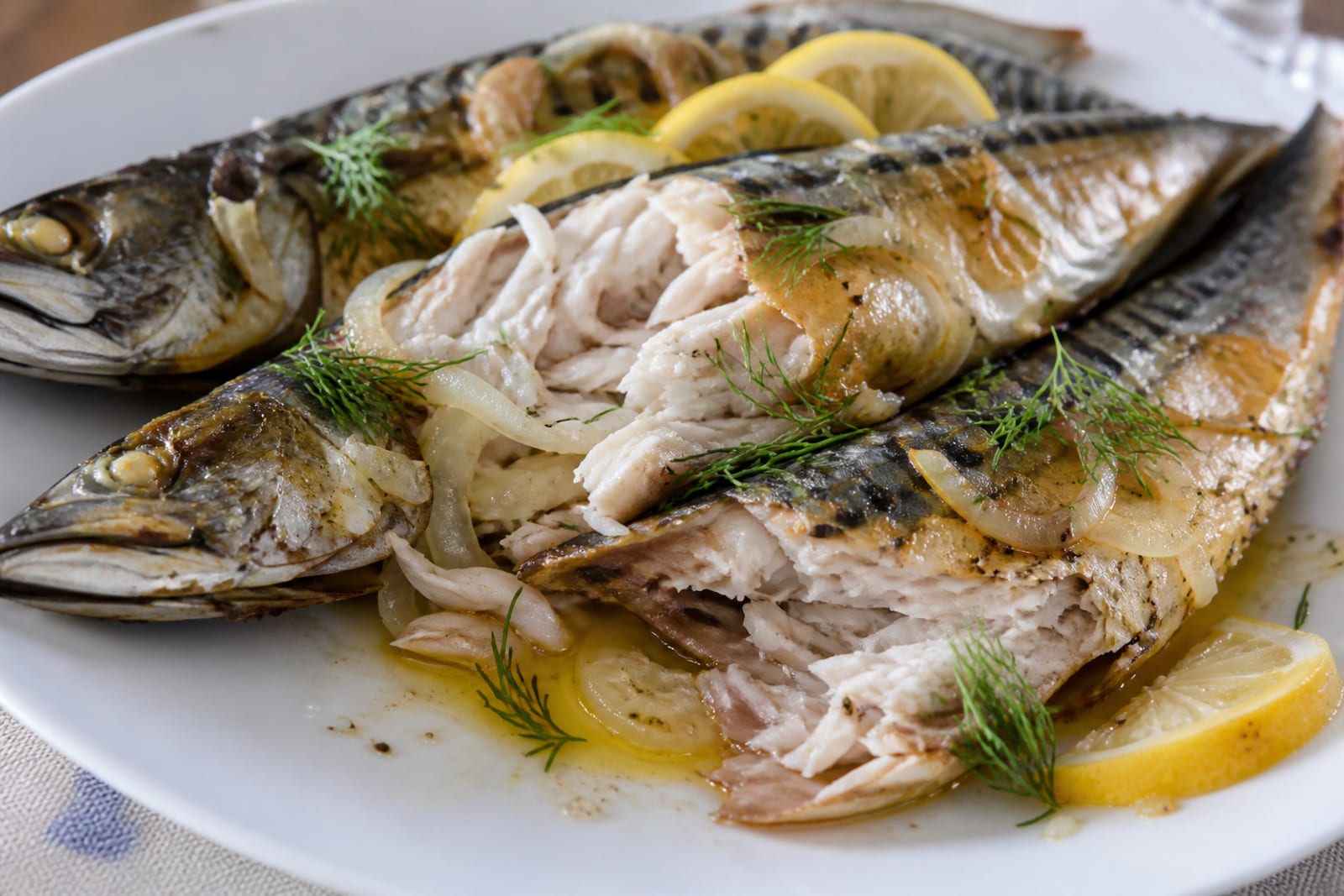 Готовая запечённая скумбрия на тарелке: мясо слоистое, лимон и укроп