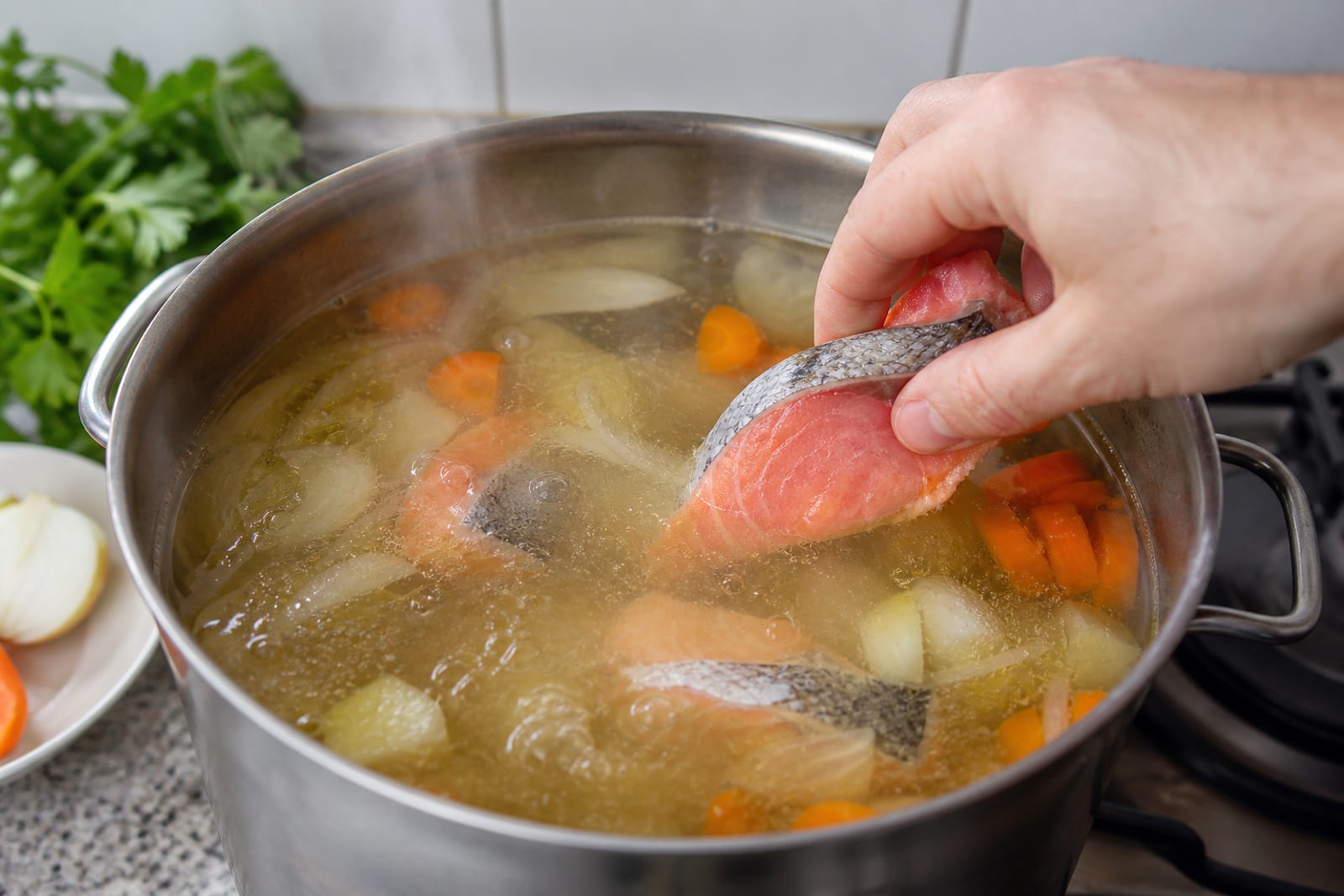 Кастрюля с прозрачным рыбным бульоном: морковь, лук и куски сёмги на плите